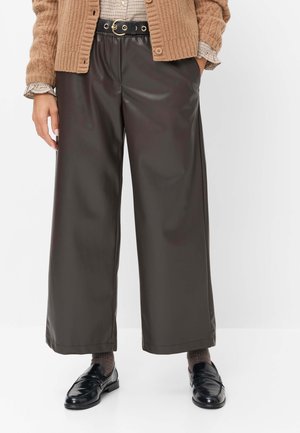 Sort læderbukser med vide ben kombineret med et brunt bælte, en beige cardigan og sorte loafers med mørke sokker.