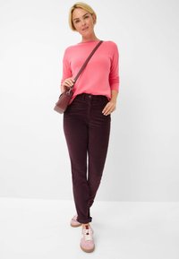 Roze trui met lange mouwen gecombineerd met donker bordeauxrode broek en lichtroze sneakers. Accessoires omvatten een kleine bordeauxrode crossbody tas.