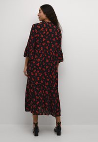 Svart blommig klänning med röda blommor, flerlagersdesign, trekvartsärmar och en flödande nederdel. Matchad med svarta klackskor med blockklack.