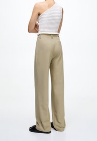 Pantaloni beige a gamba larga con una vestibilità sartoriale, caratterizzati da tasche posteriori e un tessuto liscio e leggero. Abbinati a un top bianco strutturato.