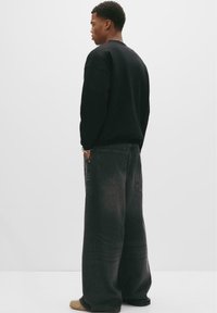 Sort sweatshirt med rund halsudskæring, parret med løstsiddende mørkegrå jeans med to baglommer. Diskret falmet tekstur på jeansene.