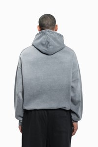 Grå oversized hettegenser med snøring i hetten, myk tekstur og senkede skuldre, kombinert med svarte løstsittende bukser.