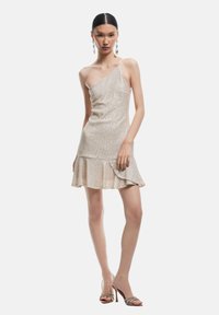 Abito beige lucido a spalla singola con corpetto aderente e orlo svasato. Texture liscia con una leggera lucentezza, abbinato a scarpe con tacchi a strappo.