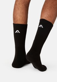 Black ribbed socks with a gray logo on the cuff. Soft texture, mid-calf length, designed to fit snugly.