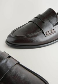 Tummanruskeat nahka loaferit, joissa on teksturoitu pinta, yläosassa oleva nauha ja koristeellinen ompelu sivussa. Kumipohja.