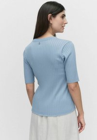 Lysblå ribbet sweater med korte ærmer, tætsiddende design, rund halsudskæring og en knapdetalje bagpå. Struktureret stof.