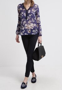 Blouse florale marine à manches longues et décolleté en V, associée à un jean skinny noir, un sac à main noir et des ballerines brodées marines.