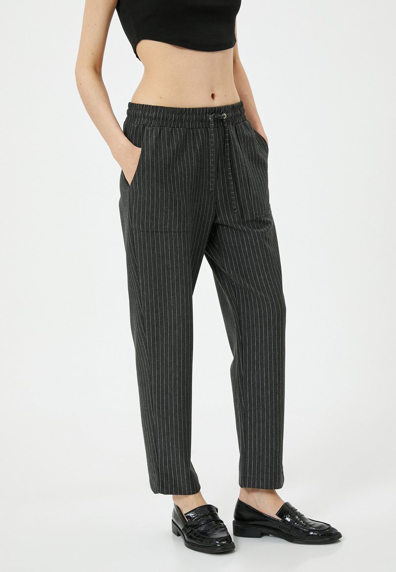 Grijze broek met streepjespatroon, een tailleband met trekkoord, zijzakken en een relaxte pasvorm. Gecombineerd met zwarte glanzende instappers voor contrast.