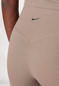 Leggings côtelés marron clair avec un logo Swoosh noir de Nike, conçus pour être ajustés et dotés d'une texture lisse.