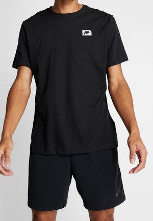 Homme portant un t-shirt noir uni Nike avec logo sur la poitrine et un short noir assorti avec le swoosh Nike sur la jambe gauche.