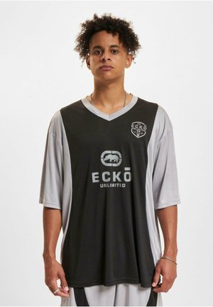 Maillot noir et gris à manches courtes avec un col en V, doté d'un logo sur la poitrine et d'une manche gauche grise contrastante. Fabriqué en tissu lisse.