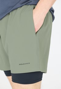 Ljust gröna träningsshorts med elastisk midja och sidofickor, med en svart innerfoder och "ENDURANCE"-logotyp nära fållen.