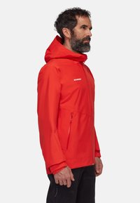Giacca impermeabile rossa con cappuccio, dotata di zip frontale, tasche laterali con zip e una texture liscia. Logo visibile sul petto.