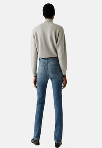 Maglione grigio a coste abbinato a jeans blu aderenti. I jeans presentano due tasche posteriori e un vita media. Scarpe nere completano il look.