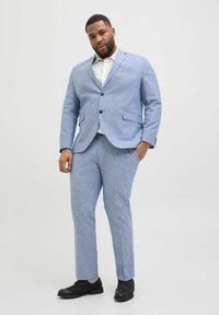 Hellblauer Anzug aus strukturiertem Stoff mit taillierter Jacke, einreihigem Design, zwei Knöpfen und passenden Hosen, kombiniert mit schwarzen Schuhen.