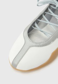 Άσπρο δερμάτινο παπούτσι με στρογγυλεμένη μύτη, γκρι λεπτομέρειες και ανοιχτό μπλε κορδόνια. Διαθέτει λεία υφή και λαστιχένια σόλα για καλύτερη πρόσφυση.