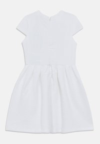 Λευκό φόρεμα με υφασματικό μοτίβο, κοντά μανίκια και φερμουάρ στο πίσω μέρος. Η φούστα έχει πιέτες για επιπλέον όγκο.