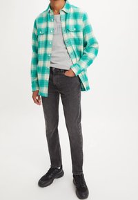 Grön- och vitrutigt flanellskjorta över en grå T-shirt, kombinerad med svarta jeans och svarta sportskor. Knäppning framtill och två bröstfickor.