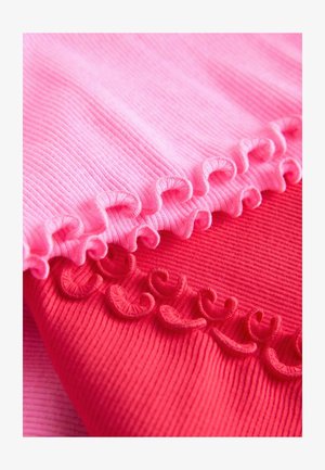 Dva komada rebraste tkanine, jedan svijetlo ružičasti i jedan crveni, s dekorativnim naboranim rubovima. Teksture su glatke i rastezljive.