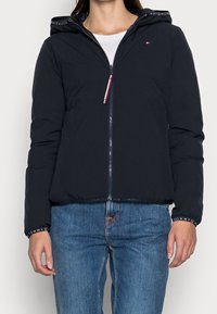 Giacca imbottita navy con zip frontale, cappuccio e accenti di logo sui polsini. Caratterizzata da una vestibilità slim e una texture liscia.