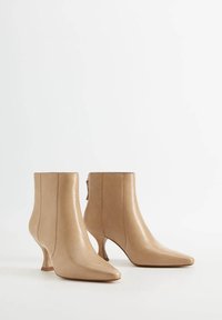 Botines de cuero beige hasta el tobillo con punta afilada, tacón curvado único, textura suave y diseño minimalista. Sin herrajes ni patrones visibles.