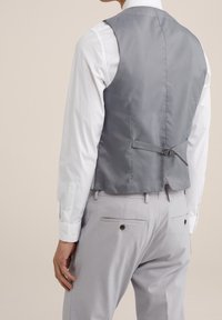 Grå satinväst med åtsittande rygg, sidjusterare och slät yta, bärs över en vit skjorta och grå byxor.