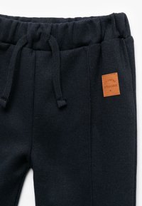 Joggers de canalé en azul oscuro con una cintura elástica, que presentan una etiqueta de cuero marrón con texto. La tela tiene una apariencia texturizada.