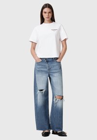 Tricou alb scurt cu logo-ul "ALLSAINTS". Blugi largi din denim cu o nuanță deschisă de albastru, tiv desfăcut și două detalii mari rupte la genunchi.