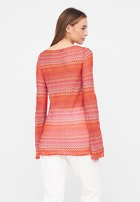 Langärmliger, taillierter Pullover im rot-pinken Zickzackmuster mit transparenter Strickstruktur. Verfügt über einen weiten Halsausschnitt und ausgestellt Bündchen.