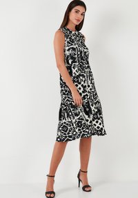 Black and white patterned sleeveless dress with a fitted bodice and flared hem, made from smooth fabric. Paired with black strappy heels.