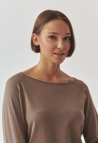 Braunes Langarmoberteil mit weitem Ausschnitt, glatter Textur und Raglanärmeln, das dezente Steppnähte an den Nähten aufweist.