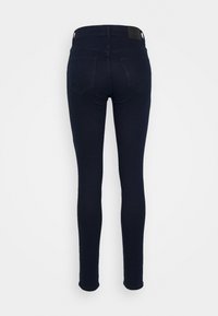 Jeans skinny de color azul oscuro exhibidos por la parte de atrás. Presentan una textura suave, dos bolsillos traseros y una etiqueta de cuero en la cintura.