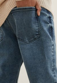 Jeans de denim azul con un acabado ligeramente desvanecido, que cuentan con un bolsillo trasero curvado y un ajuste ceñido en la cintura y las piernas.