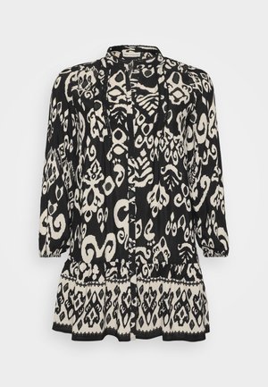 Black and white patterned long-sleeve blouse with a relaxed fit, featuring ruffled hem and button closure; made of lightweight fabric.