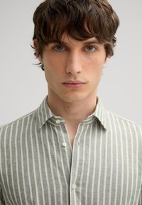 Helles grün gestreiftes Hemd mit umlegbarem Kragen, das weiße vertikale Streifen aufweist, aus strukturiertem Stoff gefertigt ist und eine standardmäßige Knopfverschluss hat.