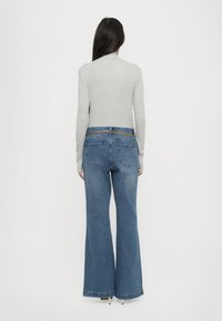 Gray long-sleeve top paired with blue wide-leg jeans featuring a chain detail along the waistband and two back pockets.