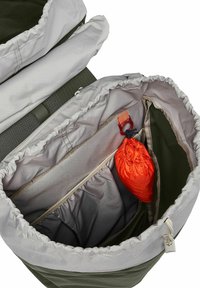Interior de una mochila verde con forro gris claro, cuenta con bolsillos con cremallera y elásticos. Incluye un pouch con cordón naranja y un llavero.