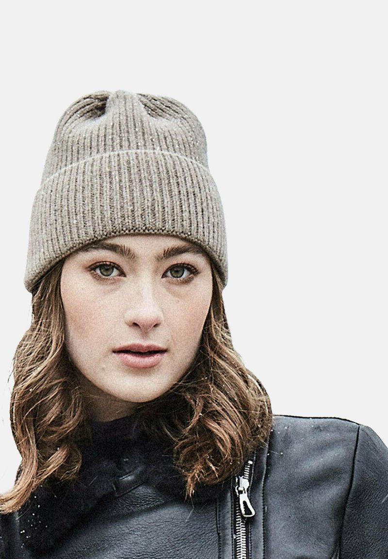 Grey knit beanie with ribbed texture, featuring a folded cuff and subtle sheen. Worn with a black leather jacket, showing a close-up view.