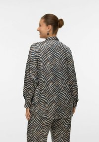 Koszula z długim rękawem w wzór zebry w kolorach granatowym, beżowym i białym. Wykonana z gładkiego materiału, z kołnierzykiem i luźnym krojem.