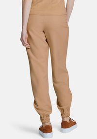 Beige joggings gemaakt van zacht materiaal met een elastische tailleband en boorden. Gecombineerd met bruine instapschoenen.