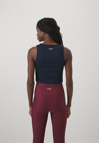 Námorná crop tank top s okrúhlym výstrihom, na chrbte so štítkom "casall", v kombinácii s nohavicami s vysokým pásom v marónovej farbe.