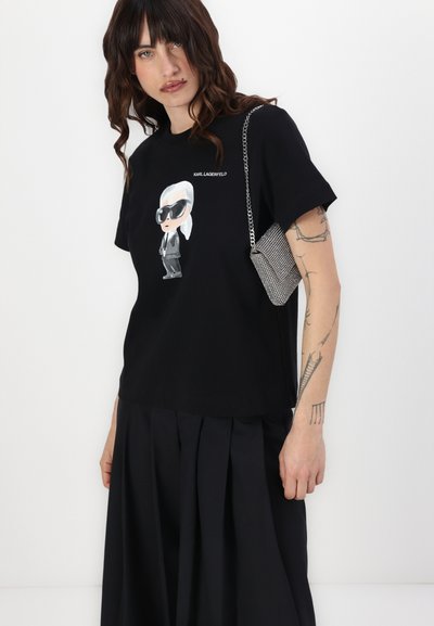 T-shirt en coton noir avec un graphique représentant un personnage portant des lunettes de soleil et un costume. Accompagné d'un sac à main en chaîne métallique, texture lisse.