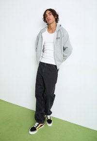 Sudadera gris con logo, camiseta sin mangas blanca, jeans de pierna ancha negros y zapatillas negras con diseño de llamas. Tejido suave y corte relajado.