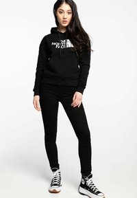 Sudadera negra con logo blanco, pantalones ajustados negros y zapatillas altas negras. Tejido suave, diseño informal y silueta ajustada.