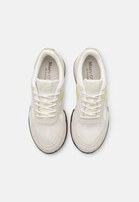 Sneaker bianche realizzate con un mix di materiali in rete e suede, con suole nere e dettagli in neon giallo sui lati e nei lacci.