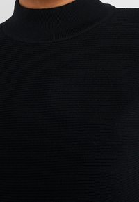 Svart ribbad turtleneck-tröja i stickat material med en åtsittande design och texturerad yta, som framhäver jämna stygn över hela plagget.