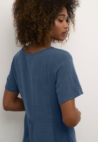 Short-sleeved, blue dress with a textured design, round neckline, and gathered waist detail. The fabric appears soft and lightweight.