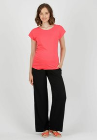 Korallfarbener Top mit Rundhalsausschnitt und kurzen Ärmeln, kombiniert mit schwarzen weitem Hosen und orangen Sandalen. Glattes Gewebe mit lockerer Passform.