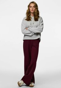 Szara krótka bluza z kapturem i sznureczkami, zestawiona z luźnymi bordowymi spodniami i kremowymi tenisówkami. Miękka faktura i swobodny krój.