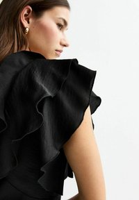 Top in tessuto nero con maniche a volant, caratterizzato da una finitura testurizzata. La vista ravvicinata mette in risalto la silhouette elegante e il morbido drappeggio.